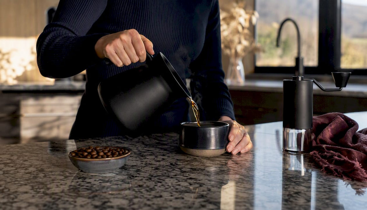 Hands pouring black coffee into cup
