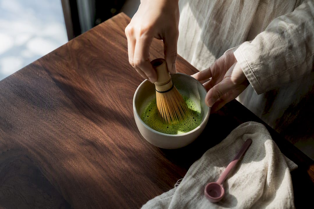 Hands whisking matcha into a ceramic bowl