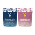 Two stand-up pouches of Emberk mushroom coffee blends on a plain white background: a dark blue pouch labeled Mushroom Coffee and a dusty pink pouch labeled Mushroom Latte. Both packages show the yellow Emberk deer logo and product text.