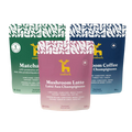Three pouches arranged together: Matcha Latte with probiotics, Mushroom Latte, and Mushroom Coffee. The front pouch is pink and labeled Mushroom Latte, with a deer logo, while the rear pouches are green and blue.